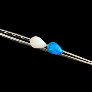 May include: Two teardrop-shaped opal gemstones, one white and one blue, are held by a silver tool against a black background. The white opal has a pearly sheen, while the blue opal displays a vibrant, swirling pattern.