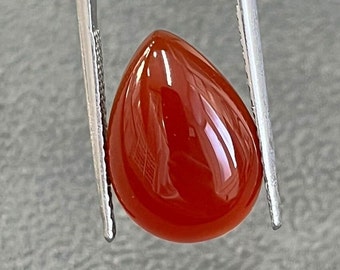 May include: A teardrop-shaped, red carnelian gemstone with a smooth, polished surface.