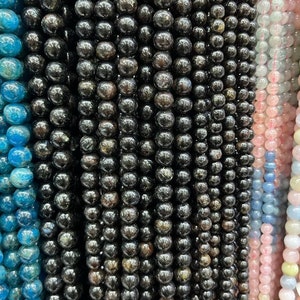 May include: A close-up of a strand of black gemstone beads. The beads are round and have a smooth, polished finish. The beads are arranged in a straight line and are evenly spaced.
