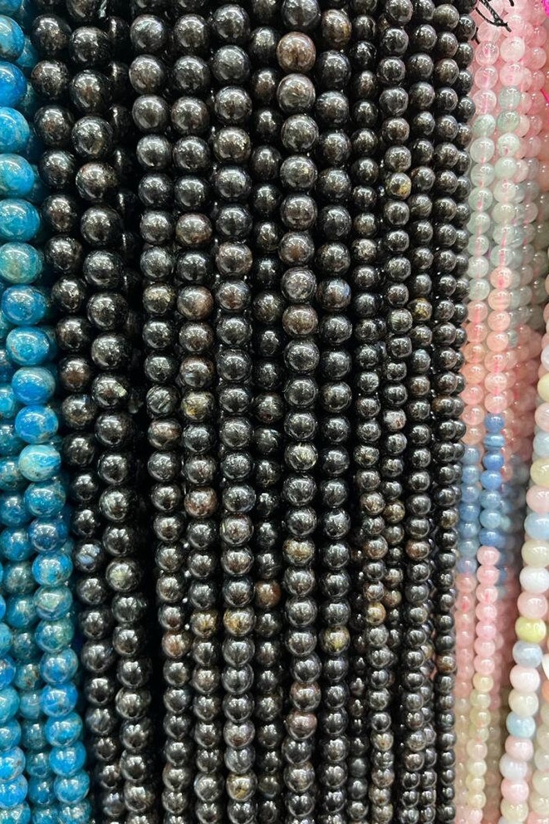 May include: A close-up of a strand of black gemstone beads. The beads are round and have a smooth, polished finish. The beads are arranged in a straight line and are evenly spaced.