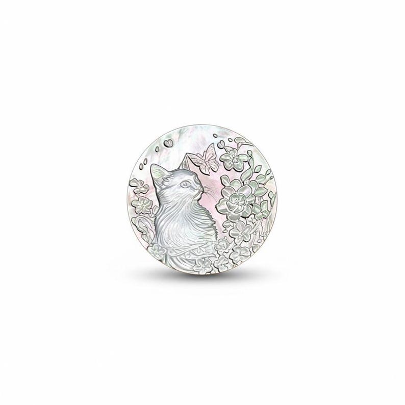 May include: A round, mother-of-pearl pendant featuring a detailed illustration of a cat gazing to the side. The design includes flowers and butterflies, with a soft pink background. The pendant has a pearlescent sheen.