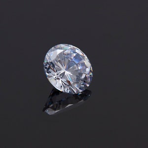 May include: A large, clear, round diamond gemstone with many facets, reflecting light on a black surface.