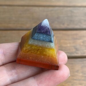 May include: A small, multi-colored crystal pyramid with seven layers. The layers are red, orange, yellow, green, blue, indigo, and violet. The pyramid is made of polished stones.