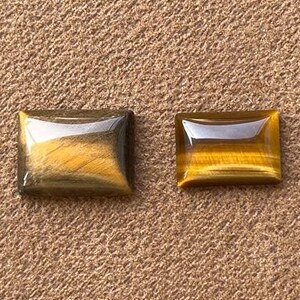 May include: Two rectangular tiger's eye gemstones, one with a darker, more golden hue and the other with a lighter, more brown hue.