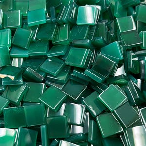 Puede incluir: Un montón de pequeñas baldosas cuadradas de color verde esmeralda. Las baldosas son brillantes y reflejan la luz, creando reflejos y sombras. Las baldosas están dispersas, lo que sugiere un proyecto artesanal.