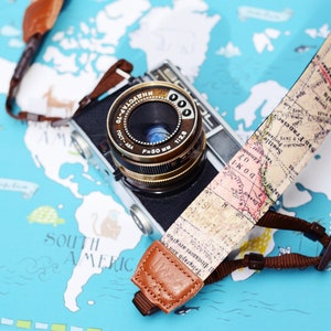 May include: A vintage camera with a brown leather strap featuring a world map design. The camera is lying on a blue and white world map background.