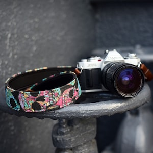 May include: A silver Canon film camera with a black lens and a colourful skull patterned camera strap.