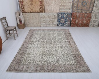 May include: A large, rectangular, vintage-style rug with a cream-colored field and a detailed floral pattern in shades of green and brown. The rug has a wide, brown border and is displayed on a light-colored floor.