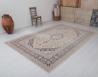 May include: A cream-colored rug with a detailed floral pattern in shades of blue, brown, and beige. The rug has a fringed edge and is laid out on a white floor.