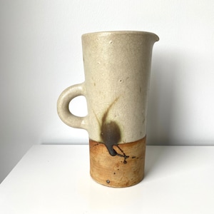 May include: A ceramic pitcher with a brown and white glaze. The pitcher has a rounded handle and a wide mouth.