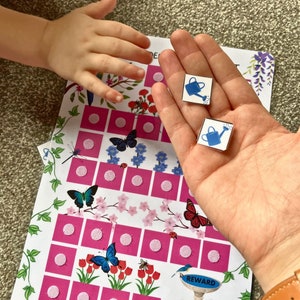 May include: A pink and white chart with a grid of circles. The chart has images of butterflies, flowers, and a watering can. The text "REWARD" is on the chart. Two blue watering can stickers are on the chart.