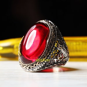 May include: A silver ring with an ornate design and a large, oval-shaped red gemstone.
