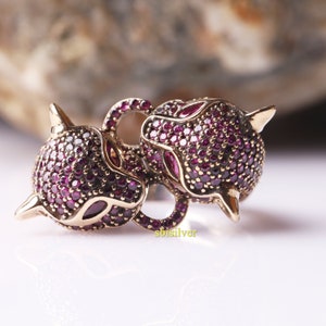 以下が含まれることがあります： 赤いキュービックジルコニアの石がついた、ゴールドトーンの動物チャームペンダント2つ。チャームは、尖った耳と長い鼻を持つスタイリッシュな動物の形をしています。