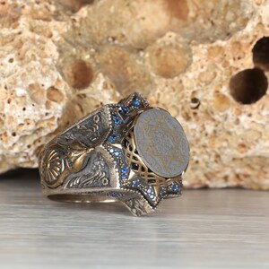 Puede incluir: Un anillo de plata con una piedra azul y un diseño de estrella de David. El anillo está engastado con pequeñas piedras azules alrededor del borde.