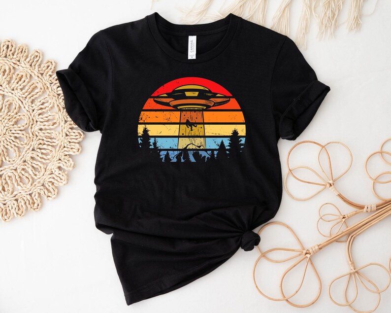 May include: Black t-shirt with a retro sunset graphic featuring a flying saucer and trees.