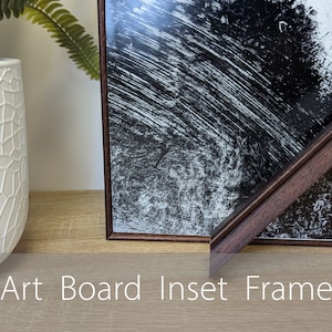 May include: A dark brown wood picture frame with a black and white abstract print inside. The frame is inset, meaning the art board is slightly recessed from the frame's edge.  Art Board Inset Frame.