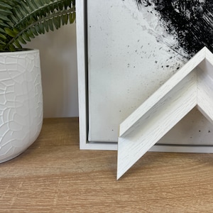 May include: White wood picture frame with a whitewashed finish. The frame is angled to show the detail of the wood grain.
