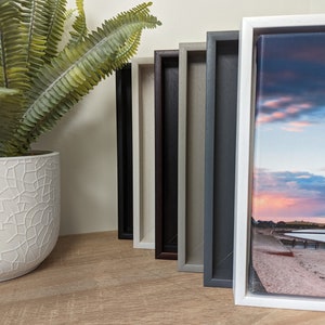 May include: Five different coloured picture frames with a canvas print of a beach scene at sunset inside the white frame.