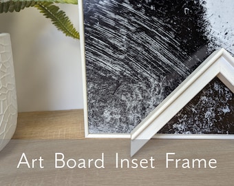 May include: White art board inset frame with a black and white abstract print. The frame is on a light wood surface.