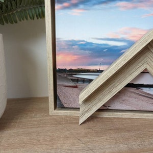 May include: A framed photograph of a beach scene with a cloudy sky at sunset. The frame is made of light wood with a natural grain pattern.