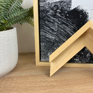 May include: Close-up of a natural wood picture frame with a bevelled edge. The frame is light brown in colour and has a smooth finish.