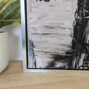May include: A black and white abstract painting with thick brushstrokes, framed in a silver frame.