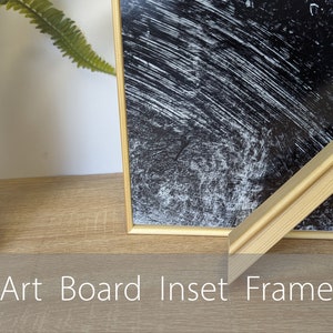 May include: A natural wood frame with a bevelled edge, showcasing a black and white abstract print. The frame is labelled "Art Board Inset Frame".