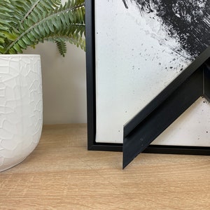 May include: A black picture frame with a wide, angled border. The frame is made of a thick, black material and has a smooth finish.