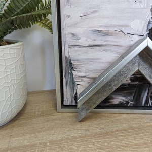 May include: A close-up of a silver and grey picture frame with a black and white abstract painting inside. The frame has a bevelled edge and a distressed wood finish.