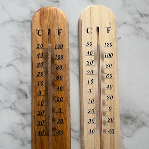 Könnte beinhalten: Zwei Holzthermometer, eines hell und eines dunkel, zeigen Celsius- und Fahrenheit-Skalen an. Die Thermometer haben eine rote Flüssigkeitssäule und sind mit Grad-Inkrementen markiert.