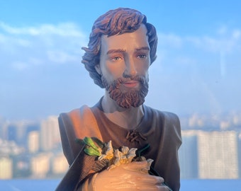 May include: A brown and tan figurine of a man with a beard holding a bouquet of white flowers. The figurine is made of resin and has a realistic appearance.