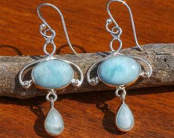 Könnte beinhalten: Silberne Ohrringe mit ovalen, hellblauen Edelsteinen und tropfenförmigen Anhängern. Die Ohrringe haben ein dekoratives Silberdesign um den ovalen Stein und einen Hakenverschluss. Die Edelsteine sind hellblau.