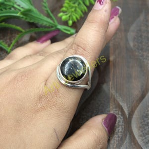 May include: A silver ring with a black and gold gemstone. The ring has a unique design with a curved band and a round setting.