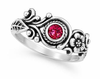 May include: A silver ring featuring a central round, faceted, vibrant pink gemstone set within a twisted rope border. The band is decorated with oxidized silver detailing, including a sculpted leaf on one side and a five-petaled flower on the other.