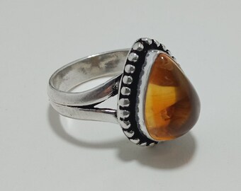 May include: A silver ring with a pear-shaped amber stone. The amber is a warm, translucent orange color, and the ring has a split shank design. The bezel setting is decorated with small, raised dots.