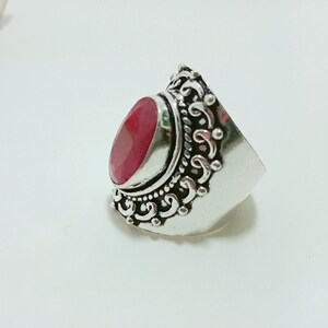 Op de afbeelding: Een zilveren ring met een ovale rode edelsteen gezet in een decoratieve zilveren band.