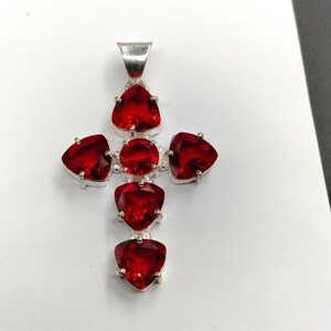 May include: A silver cross pendant with six red gemstone accents. The gemstones are triangular in shape and have a faceted cut.