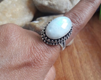 Puede incluir: Un anillo de plata con una gran piedra de luna ovalada engastada en un engaste de cuentas. El anillo está en un dedo.