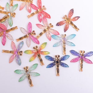 May include: Assortment of colorful dragonfly-shaped embellishments with gold accents. These decorative pieces are perfect for adding a touch of whimsy to crafts, jewelry, and other projects.