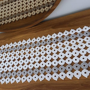 Könnte beinhalten: Weißer gehäkelter Tischläufer mit einem grauen Ombre-Design. Der Läufer besteht aus einem zarten, durchbrochenen Muster mit einer sich wiederholenden Diamantenform.