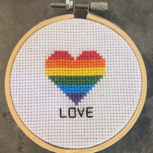 May include: A white embroidery hoop with a rainbow heart and the word "LOVE" stitched in black thread.