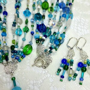 Hand crafted jewelry; four strand glass bead necklace with silver clasp, Czech rondelle charm, and earrings.
