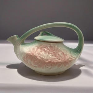 May include: A white teapot with a green handle and lid. The teapot is decorated with pink floral designs.