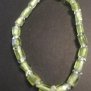 May include: A bracelet composed of light green, rectangular beads and smaller, clear, faceted beads. The beads are strung together, forming a flexible and elegant accessory. The translucent beads create a subtle shimmer.