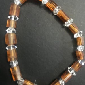 May include: A bracelet with alternating amber-coloured, rectangular beads and clear, faceted crystal beads. The bracelet is strung together, creating a flexible and decorative accessory. The beads are arranged in a repeating pattern.