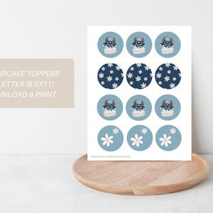May include: Printable cupcake toppers featuring a blue and white floral design and a blue character with a crown. The text "12 CUPCAKE TOPPERS US LETTER (8.5x11) DOWNLOAD & PRINT" is at the top of the page.