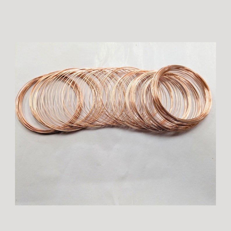 May include: A collection of multiple thin, circular copper wire coils arranged in an overlapping horizontal row. Each coil consists of several continuous loops of metallic, reddish-brown wire, creating a series of interconnected, rounded shapes.