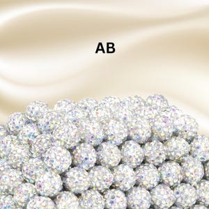 May include: A collection of round, spherical beads covered in small, clear, iridescent crystals that reflect multiple colors. The beads are arranged in a dense pile, and the letters AB are printed in black above the cluster of sparkling items.