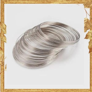 May include: A stack of multiple thin, circular silver-colored metal wire bangles. The bangles are arranged in a slightly overlapping, angled formation, showcasing their smooth, reflective surface and uniform, slender, round-profile construction.