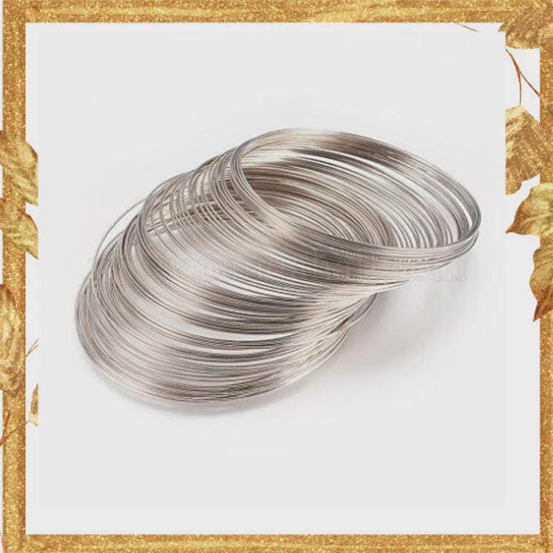 May include: A stack of multiple thin, circular silver-colored metal wire bangles. The bangles are arranged in a slightly overlapping, angled formation, showcasing their smooth, reflective surface and uniform, slender, round-profile construction.
